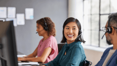 Smiling woman with headset in office providing customer support with team in background